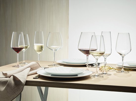 Table dressée avec six verres à vin, dont trois remplis de vin rouge et blanc, deux de champagne et un vide.