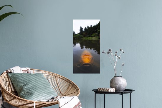 Une grande carpe koï orange nage dans un étang avec des arbres en arrière-plan.