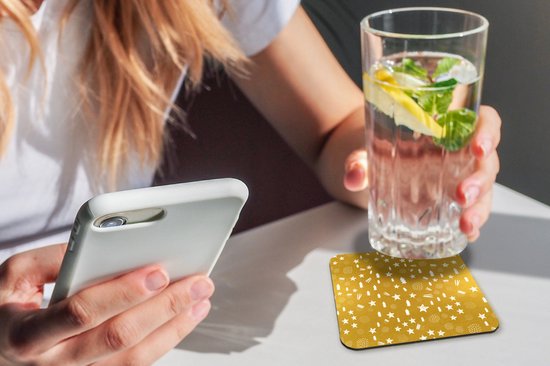 Une femme tenant un téléphone tient un verre de boisson, à côté d'un sous-verre doré à motif de Noël blanc.