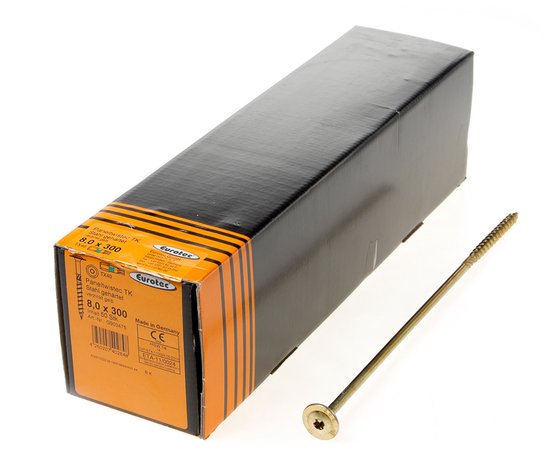 Une longue vis dorée à tête plate, à côté d'une boîte noire et orange avec des informations sur le produit.