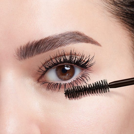 Close-up van een oog dat wordt opgemaakt met een zwarte mascara borstel voor volumineuze wimpers.