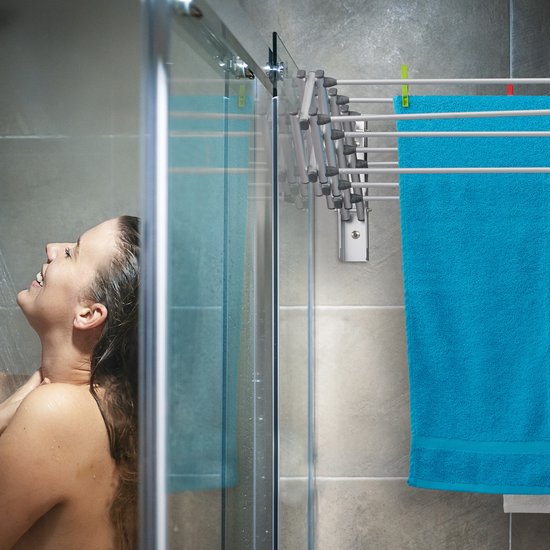 Vrouw onder de douche naast een zilverkleurig inklapbaar droogrek met een blauwe handdoek.