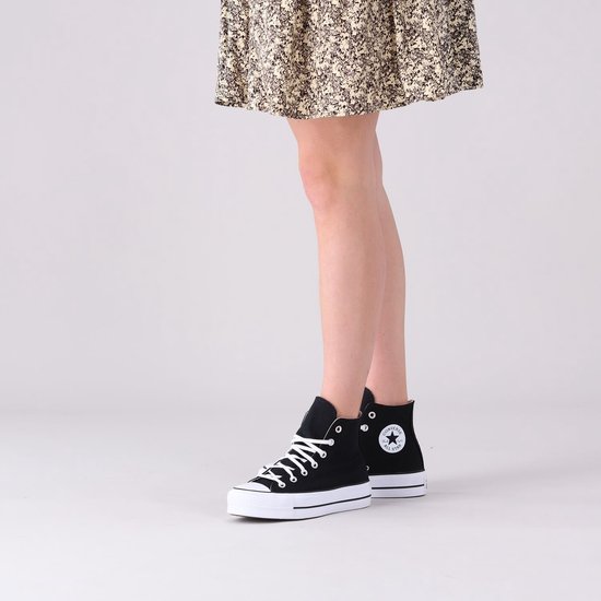 Model in een zwarte Converse Chuck Taylor All Star Lift sneakers met witte veters en een dikke witte zool, gecombineerd met een jurk.