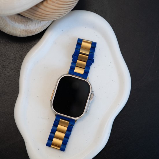 Apple Watch met een blauw en goudkleurig metalen bandje op een witte schaal.