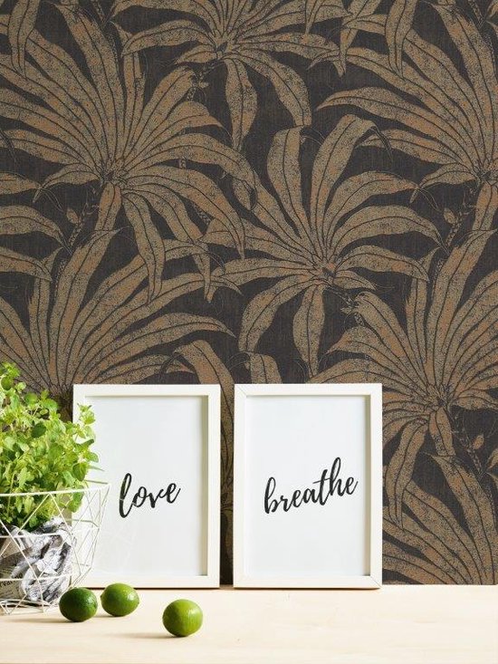 Een woonkamer met een muur behangen met gouden en bronzen junglebladeren, naast een grijze bank en twee lijsten.