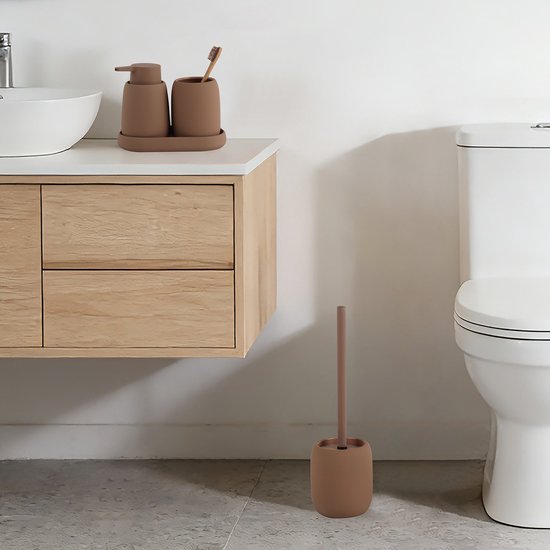 Badkamerinrichting met een bruine zeepdispenser, beker met tandenborstel en toiletborstelhouder.