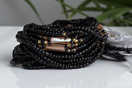Dichte stapel zwarte, niet-elastische waist beads met goudkleurige kralen en twee rechthoekige, bruin-grijze accentkralen.