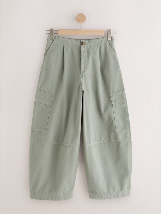 Olijfgroene cargo jeans met ballonpijpen hangend aan een kapstok.