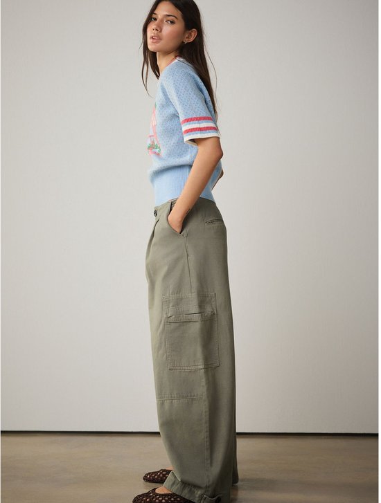Model van opzij in een olijfgroene wijde cargo broek, gecombineerd met een lichtblauwe trui.