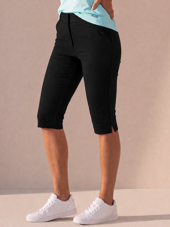 Model in zwarte capribroek tot net boven de knie, met splitjes aan de zijkanten en witte sneakers.