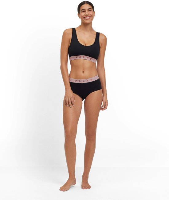 Een vrouw staat in een zwarte sportbeha en broek met roze FALKE-band.