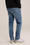 Man die een zwarte sweater en een blauwe jeans met lichte wassing draagt, gezien vanaf de zijkant.