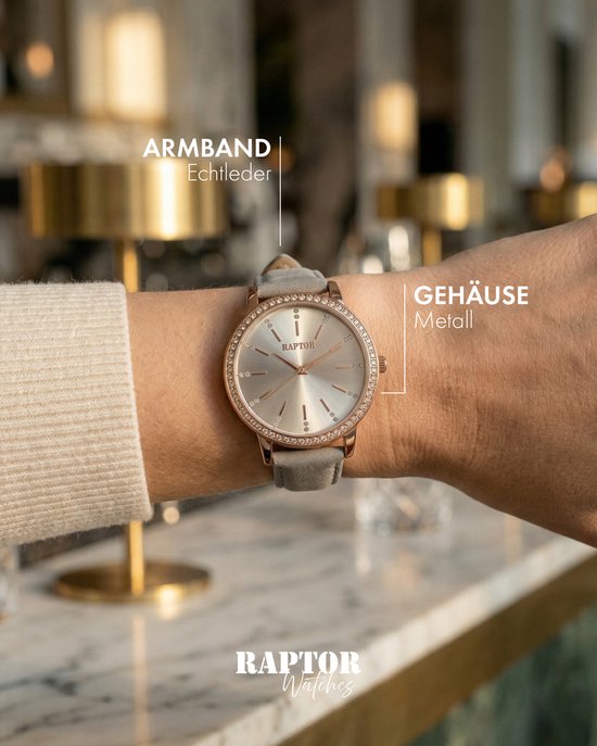 Vrouwenpols met Raptor horloge met grijze leren band en goudkleurige kast, aanduidingen voor Echt leder en Metaal.