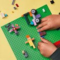 Kind bouwt met LEGO stenen op een groene bouwplaat. Met LEGO auto en figuurtjes.
