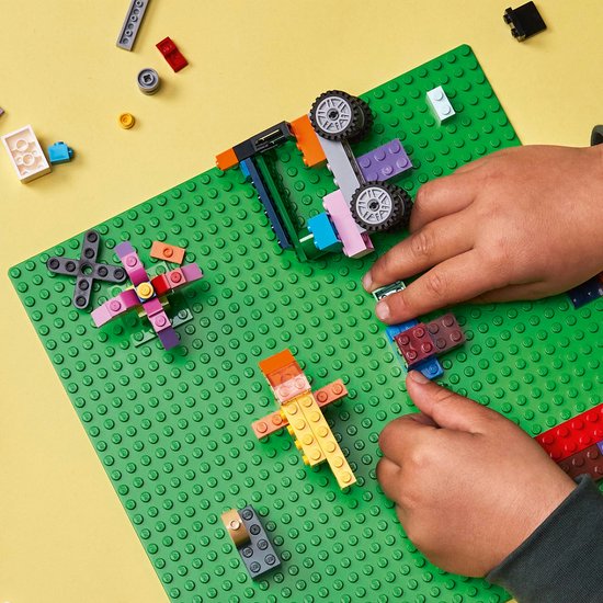 Kind bouwt met LEGO stenen op een groene bouwplaat. Met LEGO auto en figuurtjes.