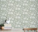 Lichtgroen behang met een delicaat wit bloemen- en bladerenpatroon, getoond op een muur met een houten tafel.