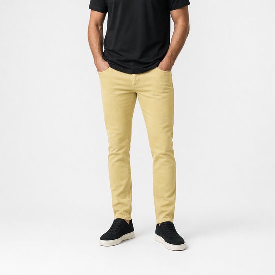 Onderlichaam van een man in een gele corduroy broek en zwarte sneakers, handen in de zakken.
