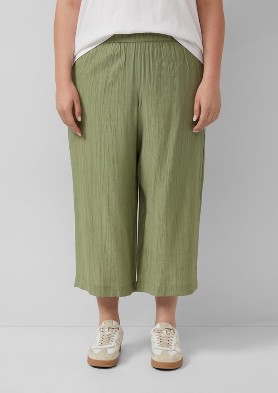 Model draagt olijfgroene culotte met crinkle stof en witte sneakers, close-up van de broekspijpen.