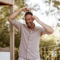 Man met bruine hemd kamt zijn haar met een kam, buiten bij een houten rek.
