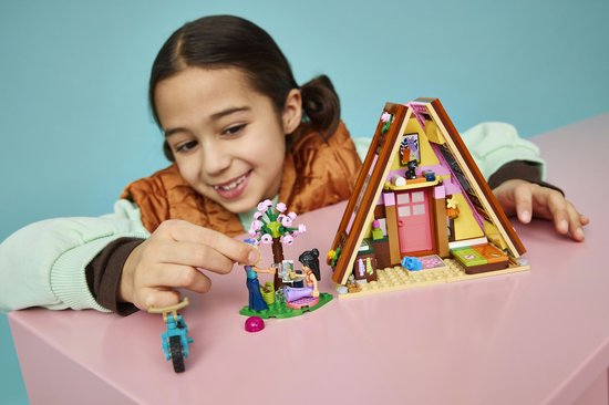 Kind kijkt glimlachend naar een Lego Friends speelgoedhuisje met roze accenten op een roze tafel.