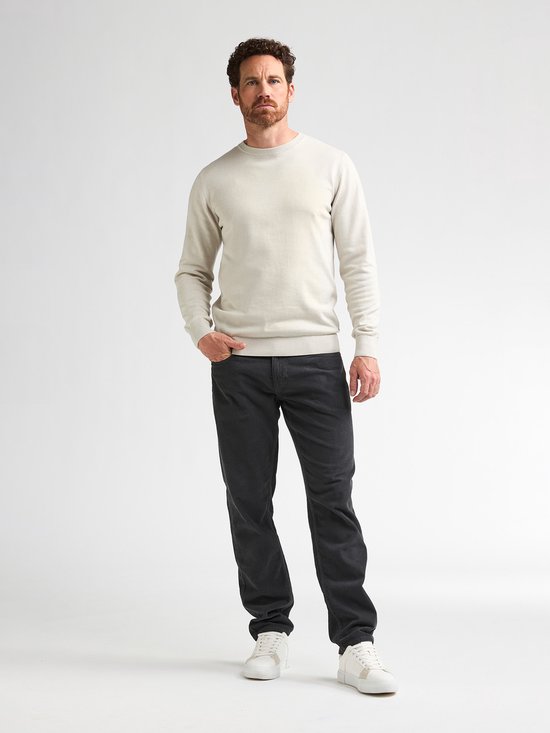 Man met beige trui met lange mouwen, handen in de zakken, van voren gezien.