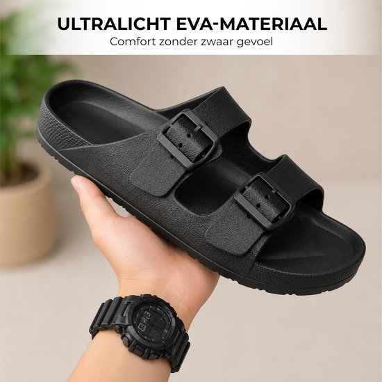 Hand houdt een zwarte slipper met dubbele gespen vast. Er wordt een zwart horloge gedragen.