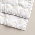 Detail van een wit dekbed met beige, herhalende bladmotieven en doorgestikte golven.
