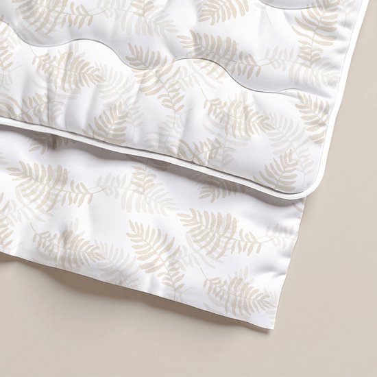 Detail van een wit dekbed met beige, herhalende bladmotieven en doorgestikte golven.
