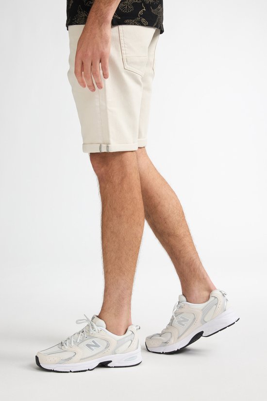 Voet van een man in beige shorts en witte sneakers.