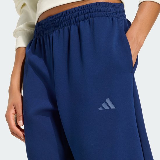 Detail van een donkerblauwe trainingsbroek met een Adidas logo op de linker heup.