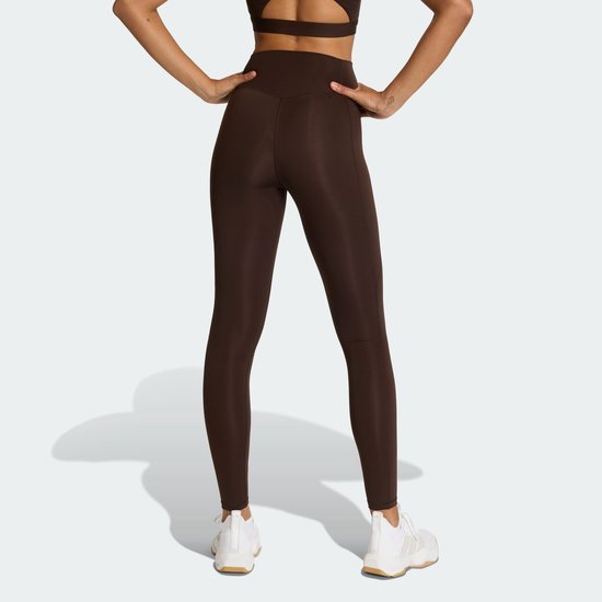 Achterkant van vrouw in donkerbruine legging, middenhoog getailleerd, witte sneakers.