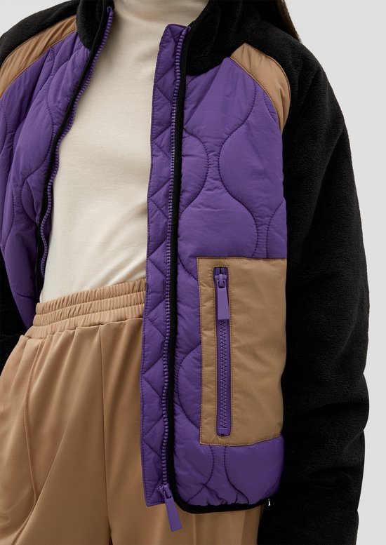 Detailopname van een gewatteerd jack in paars en bruin met een zwarte ritssluiting en fleece mouwen.