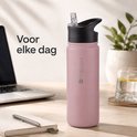 Roze 500ml drinkfles met rietjesdop op een bureau, naast laptop en glas water.
