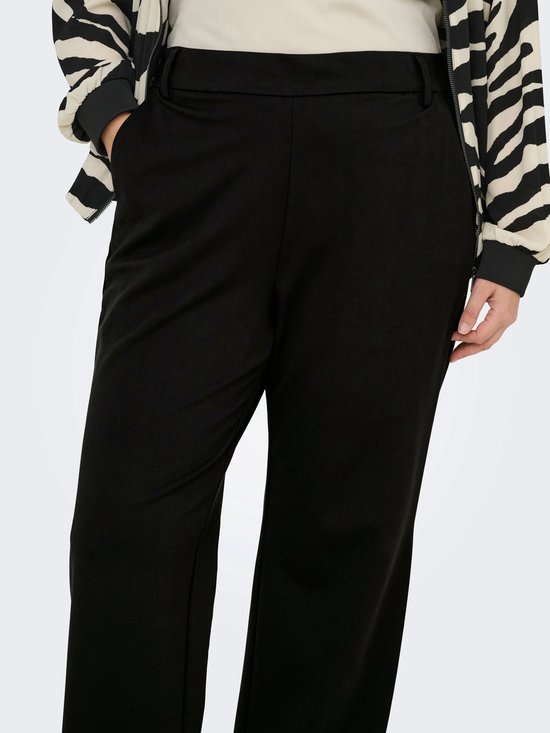 Close-up van de heupen van een model met een zwarte wijde broek en een jasje met zebraprint.