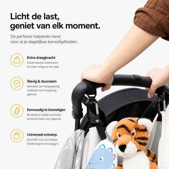 Een hand bevestigt zwarte BOTC haken aan een kinderwagen, met speelgoed en tassen eraan.