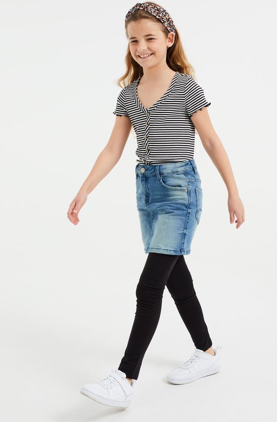 Meisje in een gestreepte top, spijkerrok en zwarte legging.