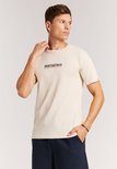 Man met zandkleurig t-shirt met korte mouwen en opdruk 'PROTEST&CO PREMIUM SURF BRAND SINCE '93' op de borst.