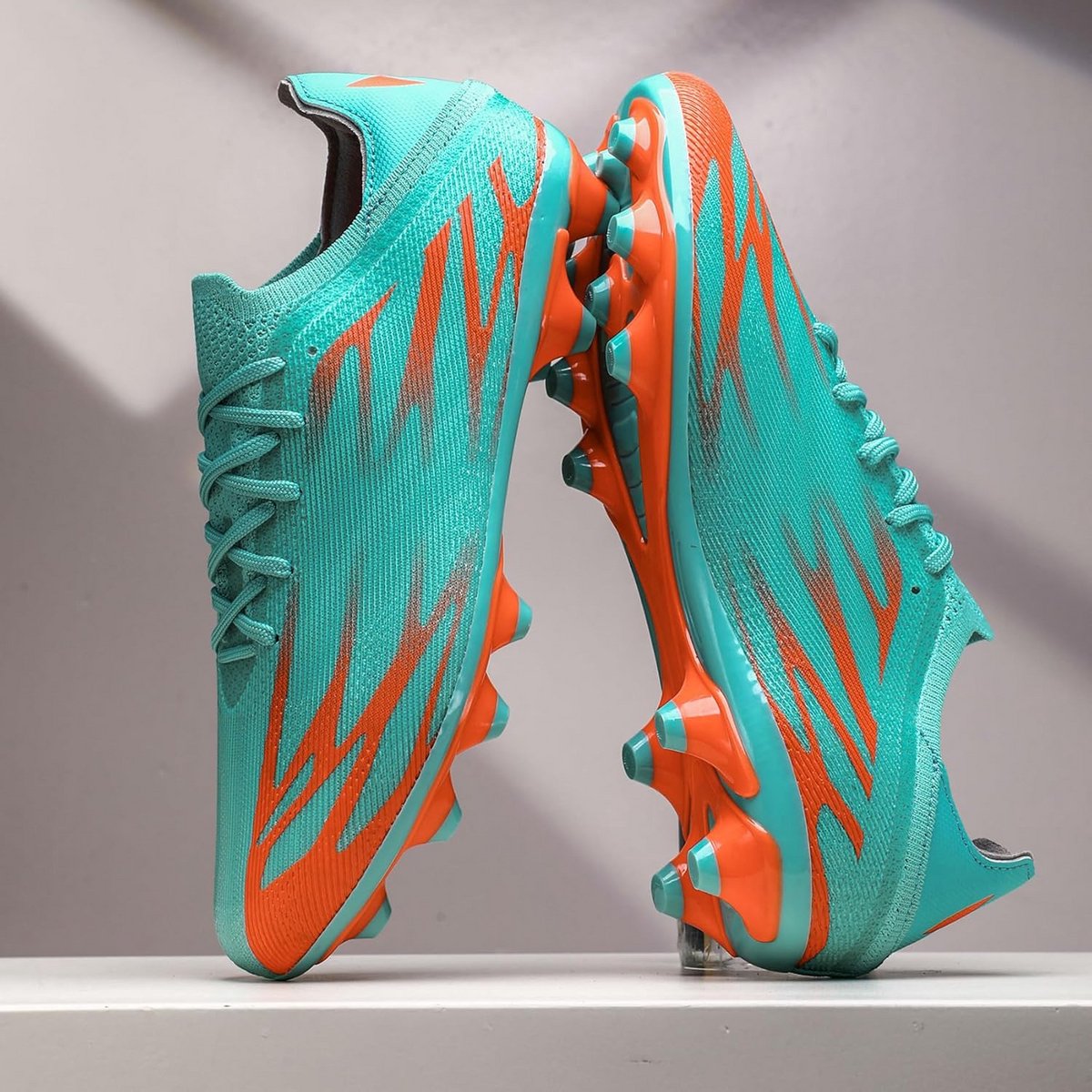 Professionele heren voetbalschoenen in turquoise met oranje details en noppenzolen voor optimale grip op grasvelden.