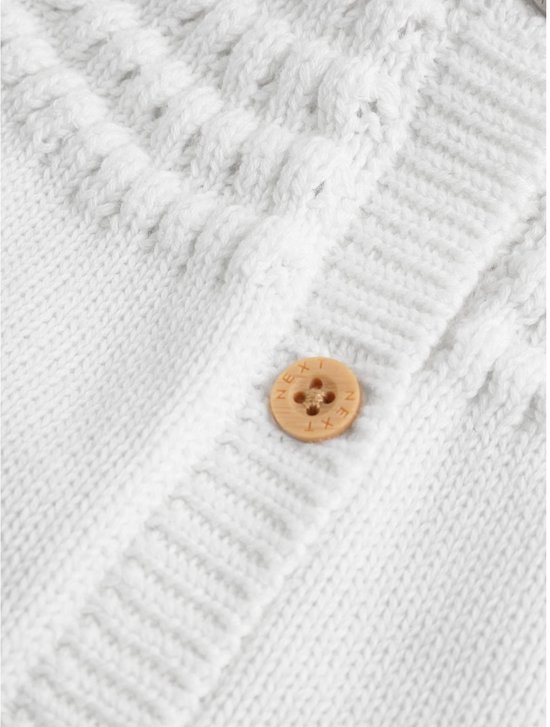 Sluiting van witte babyvest met houten knoop en gebreide kabeldetails.