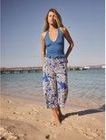 Model staat op het strand, draagt een blauwe crop top en een culotte met blauwe en crème paisley print.