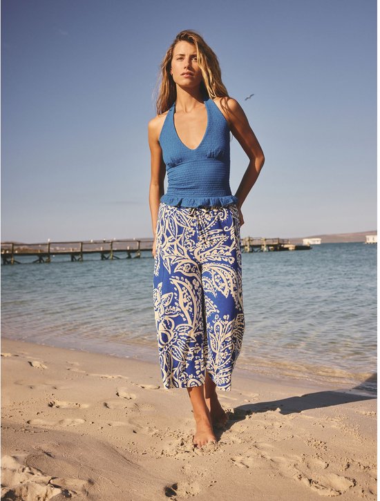 Model staat op het strand, draagt een blauwe crop top en een culotte met blauwe en crème paisley print.