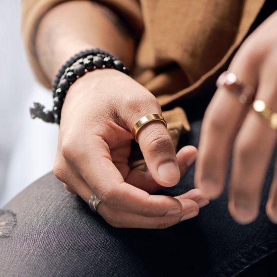 Dichtbij van een hand met gouden ringen en zwarte kralen armband.
