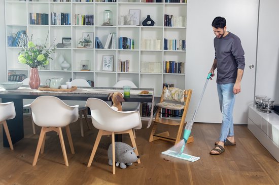 Man met Leifheit Easy Spray XL vloerwisser in een woonkamer met witte boekenkast.