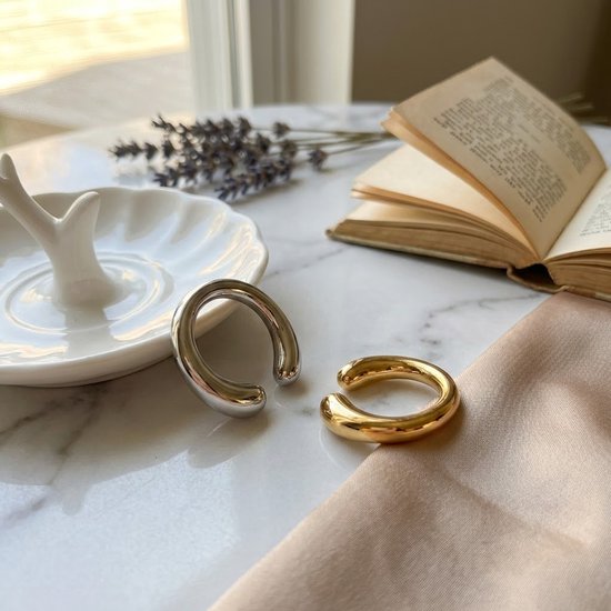 Goudkleurige en zilverkleurige ear cuffs op een marmeren tafel naast een boek en lavendel.