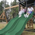 Twee kinderen glijden van een groene dubbele glijbaan op een speeltoestel.