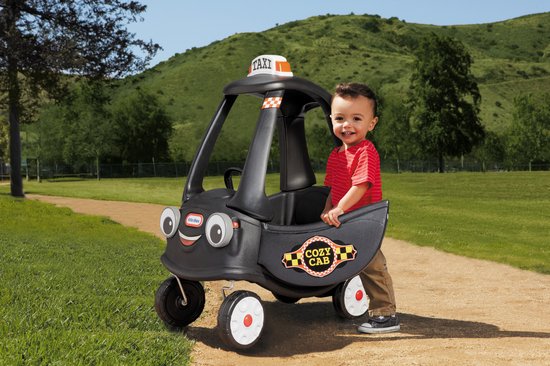 Jongen in rood gestreept shirt en bruine broek staat naast een zwarte Little Tikes Cozy Coupe Taxi met gezicht, 'COZY CAB' logo en 'TAXI' bord.