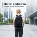 Een vrouw met blonde staart, in zakelijke kleding, draagt een zwarte rugzak in een stedelijke omgeving.