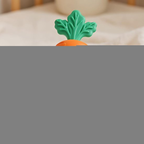 Oranje wortelspeeltje met groen blad, zacht van kleur op de achtergrond.