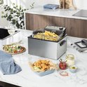 Gouden frietjes in een frituurmand in een roestvrijstalen frituurpan, naast een salade en gefrituurde kip.