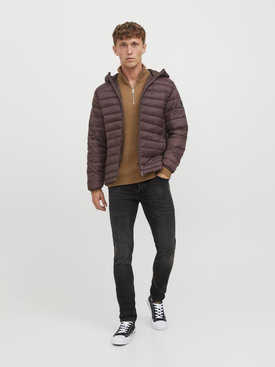 Man in een bruine gewatteerde jas, beige trui en donkere jeans, frontaal.